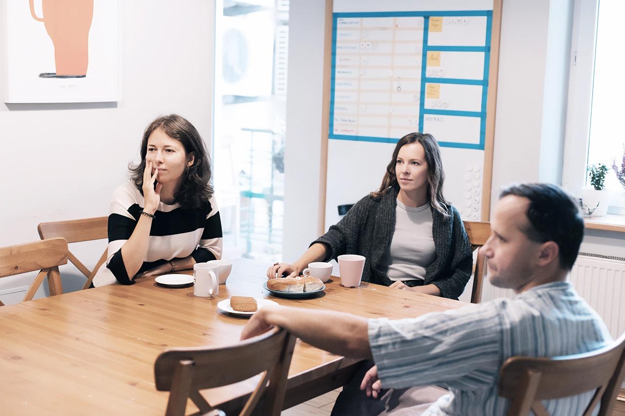 Two women and one man listening carefully to a person in the office kitchen